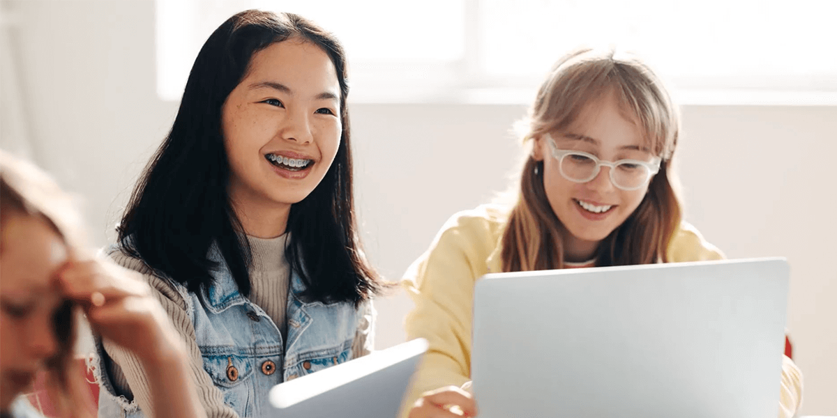 Two females sitting next to each other in front of laptops