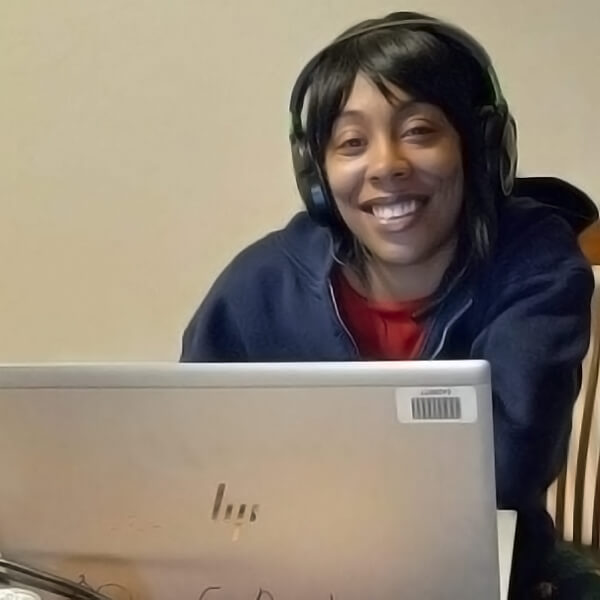 Josie wears a headphones and sits at an office desk using a laptop computer