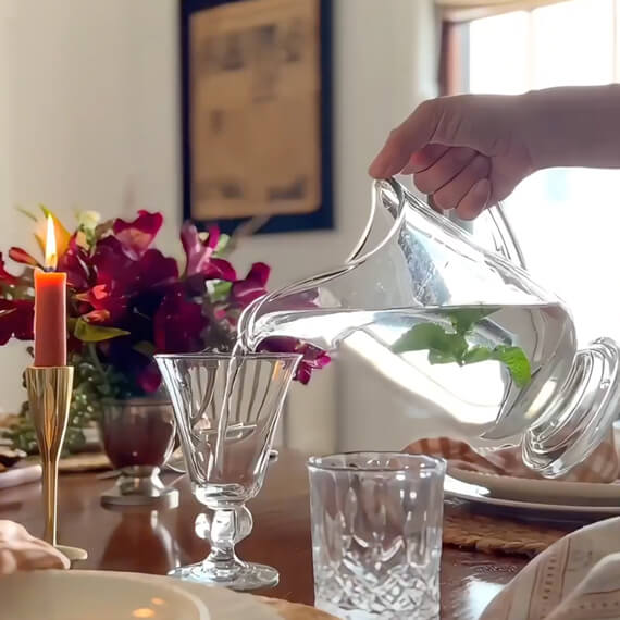 A lit candle, glassware and a pitcher a water. 