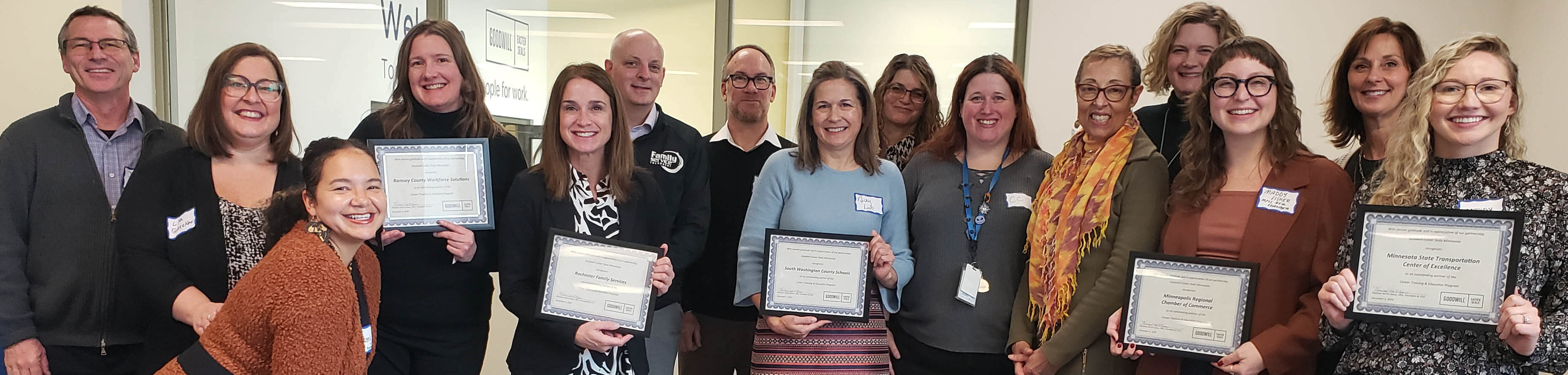 group of 15 men and women posing with 5 holding framed certificates honoring their organization's partnerships with GESMN