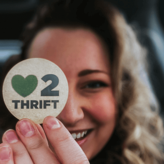 A female holding a "Heart2Thrift" sticker in hand