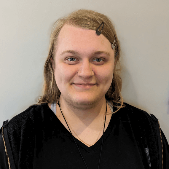 female standing in front of a beige wall with hair berets in her hair wearing a black zip up and shirt