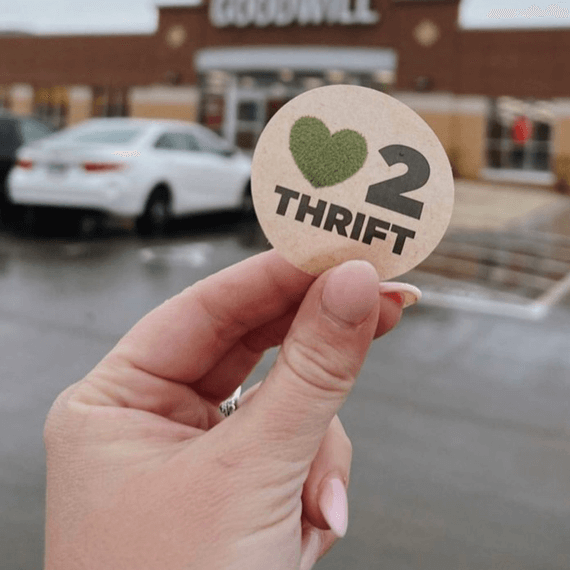 A person holding a "Heart2Thrift" sticker in hand