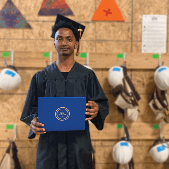 A male in a graduation cap and gown, holding a diploma in his hands.