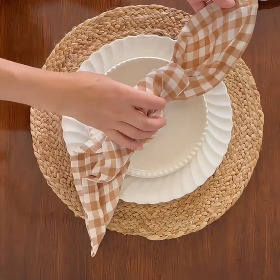 A tan place mat, two white plates and a tan and white gingham tied napkin