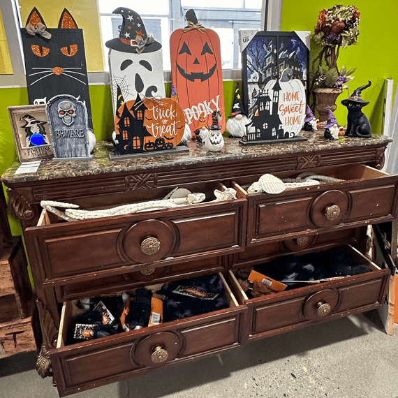 A dresser decorated for Halloween, showcasing items like bats, pumpkins, and eerie ornaments, contributing to a festive look.