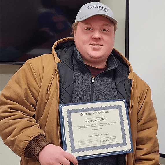 A male smiling while holding a certificate in his hands